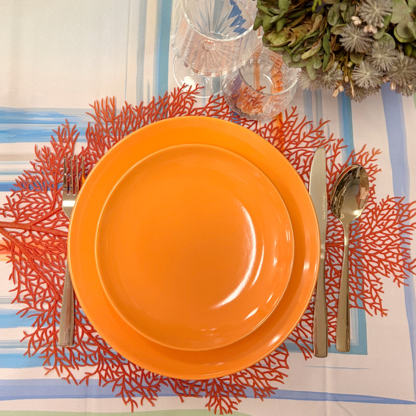Sottopiatto traforato a forma di corallo marino rosso con i piatti moderni color albicocca per un mise en place estiva e chic
