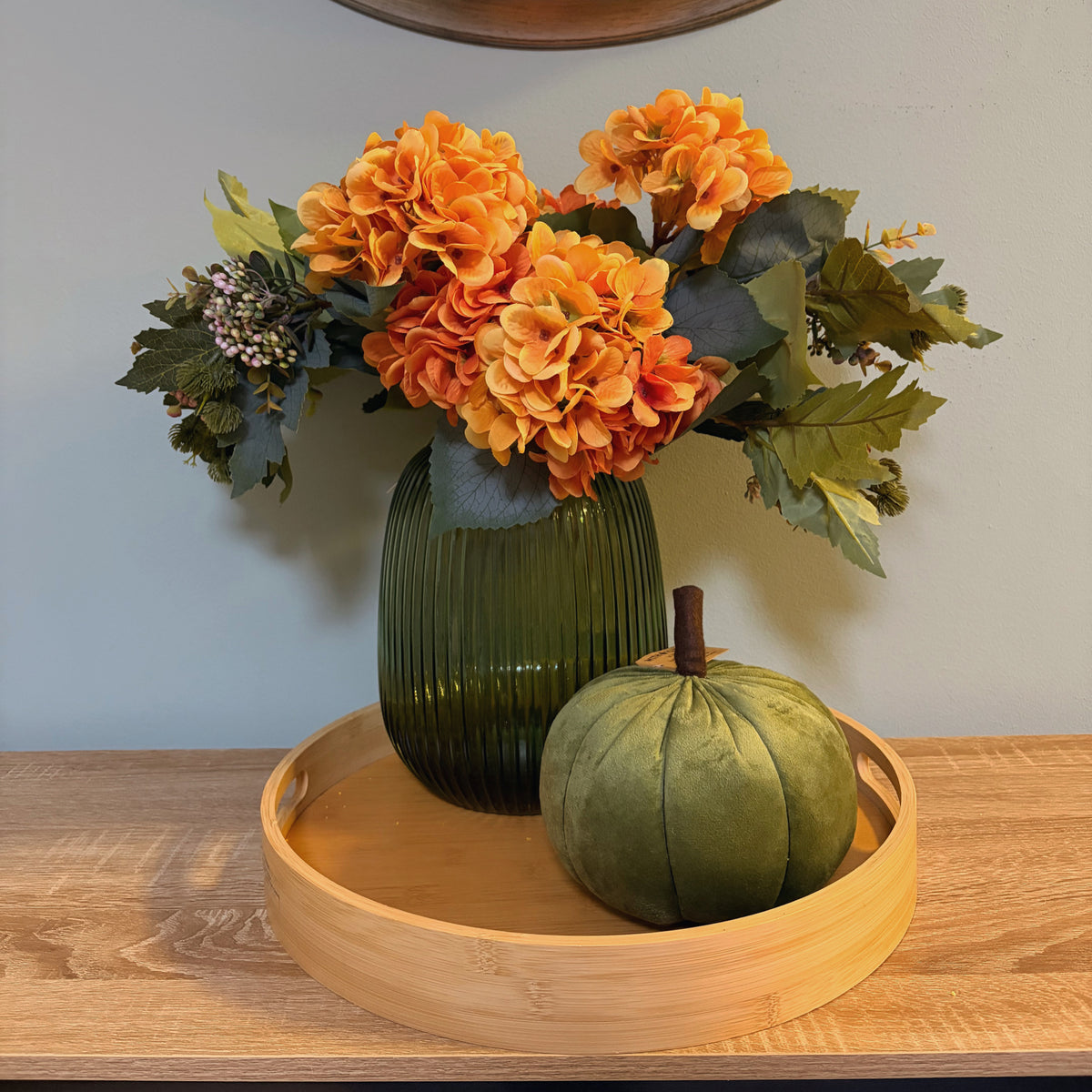 Zucca decorativa in velluto verde oliva ambientata su vassoio in legno con vaso e fiori autunnali