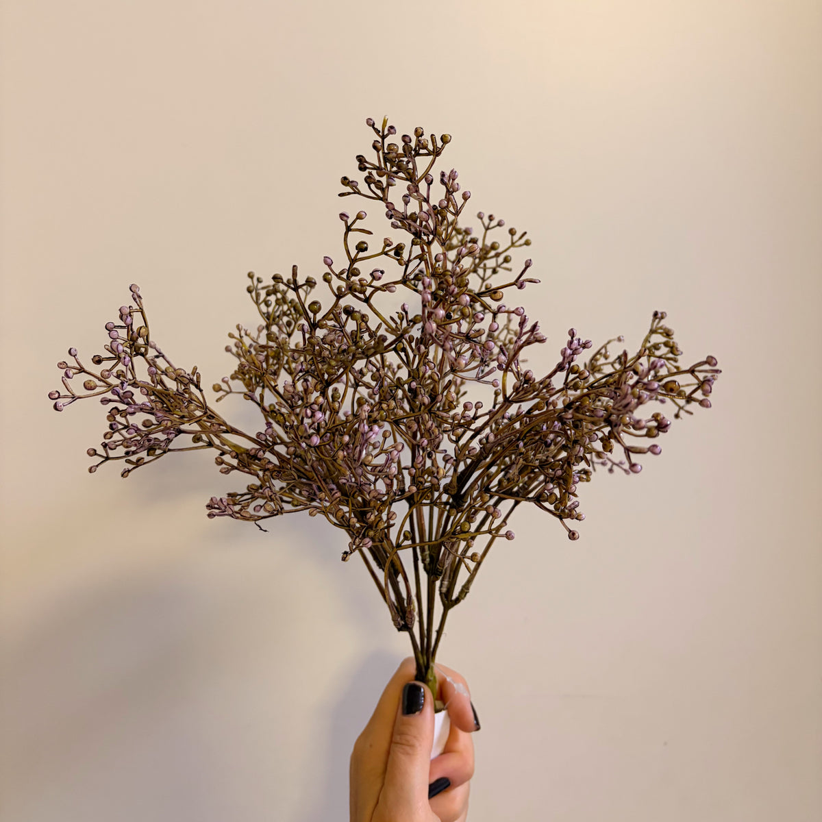 Mazzo di gypsophila artificiale di colore viola intenso ad effetto essiccato tenuto in mano per decorazioni d'interni.