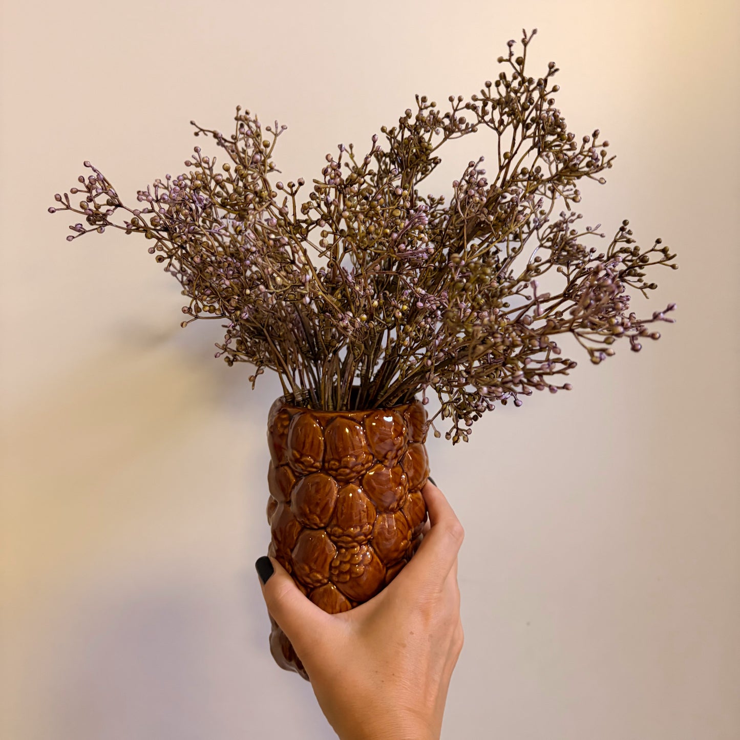 Rami di gypsophila finta color viola inseriti all'interno del vaso in ceramica marrone a forma di pigna come centrotavola autunnale.