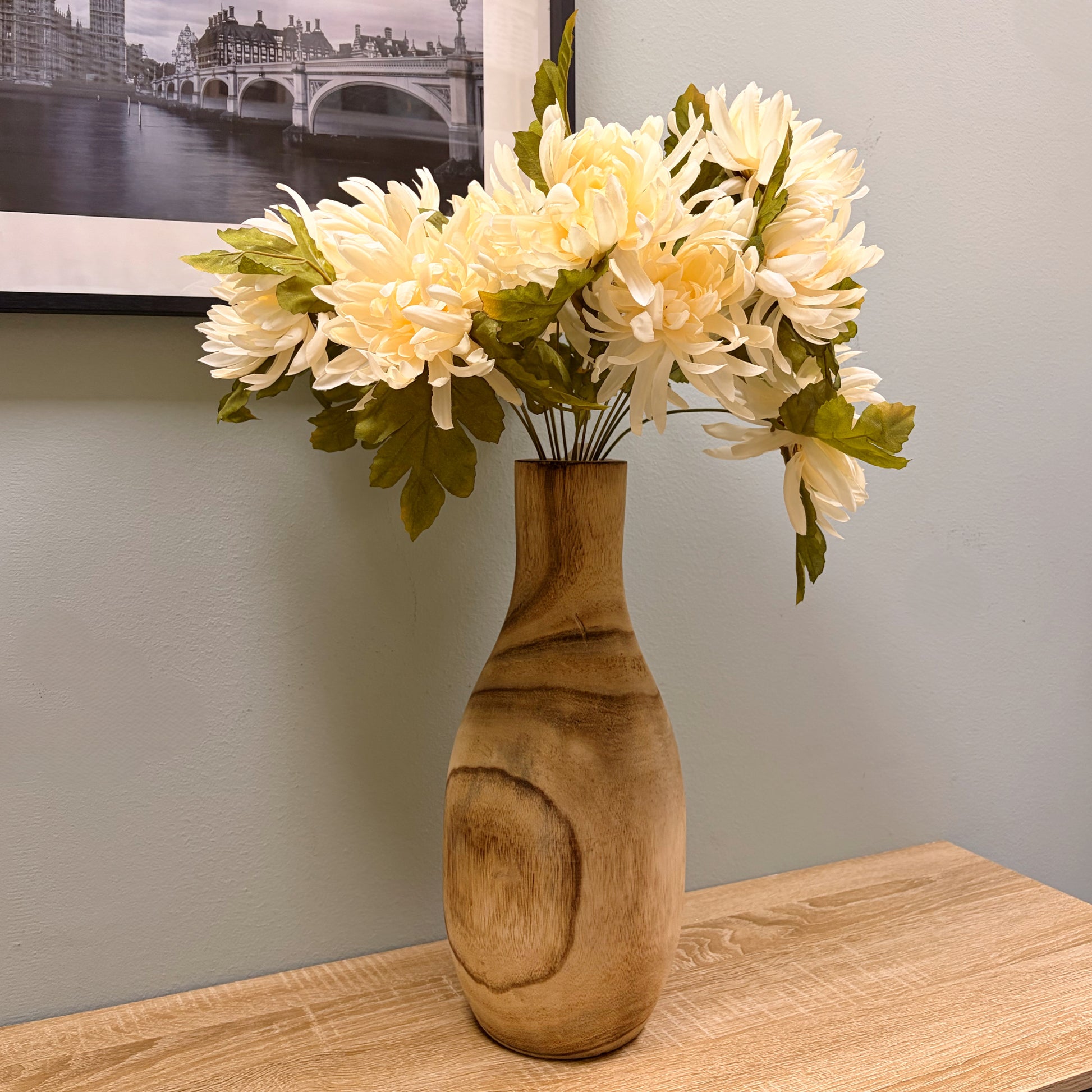Composizione floreale con fiori finti bianchi all'interno di un vaso in legno chiaro grande, appoggiato su una console.