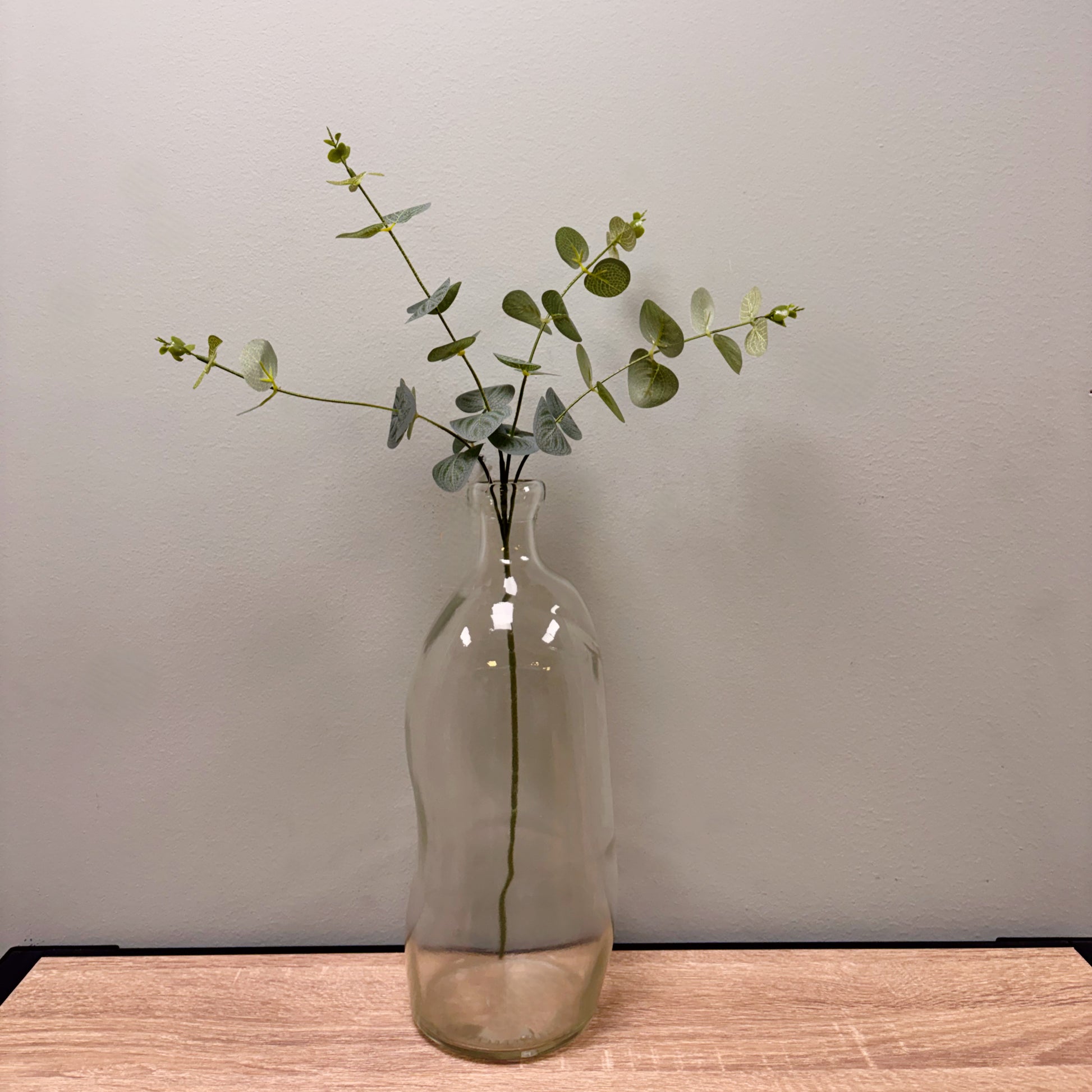 Vaso a palloncino in vetro trasparente con ramo di eucalipto su tavolo in legno - decorazione casa moderna.